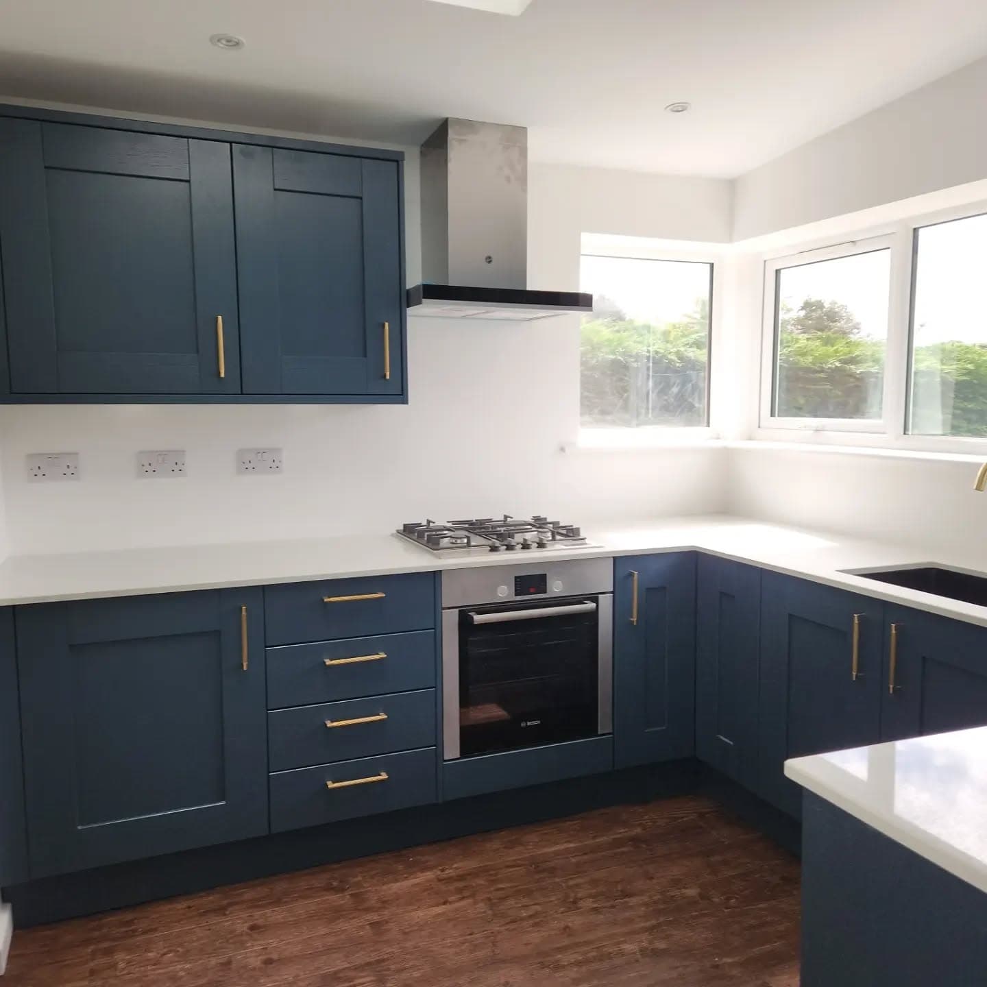 Completed kitchen with blue cabinets, white worktops and corner windows