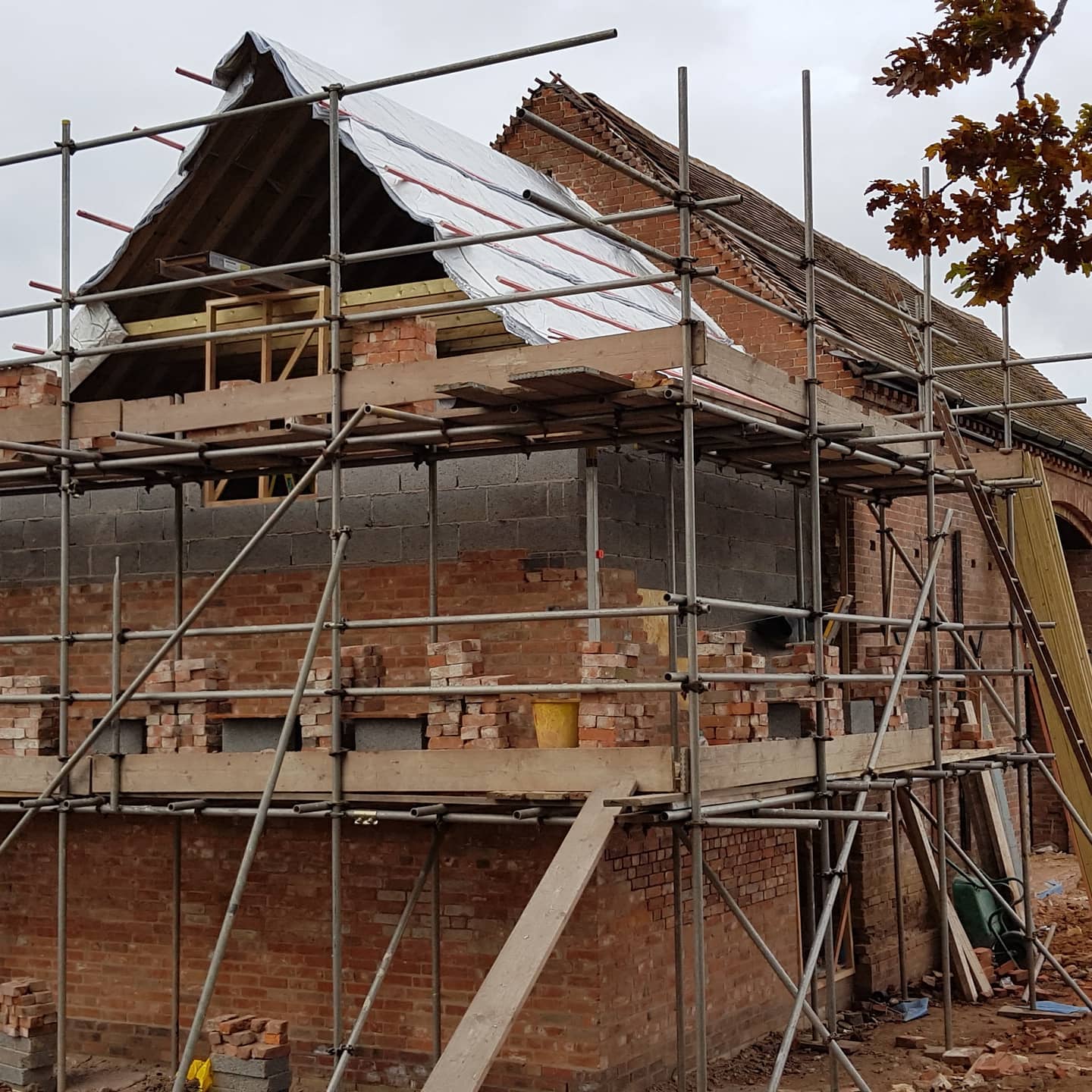 Brick house renovation in progress with scaffolding and roof construction